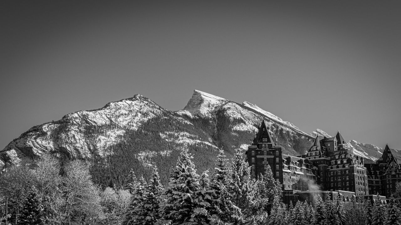 Dramatic black and white photo of a mountain scene with a historic hotel.
